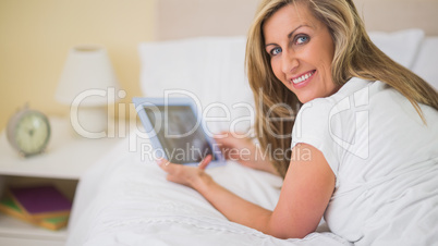 Happy woman using a tablet pc lying on her bed