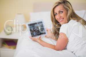 Pleased woman using a tablet pc lying on her bed