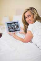 Content woman using a tablet pc lying on her bed