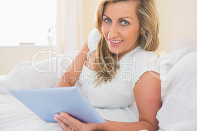 Satisfied woman looking at camera using a tablet pc lying on her