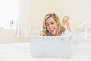 Laughing woman using a laptop lying on her bed