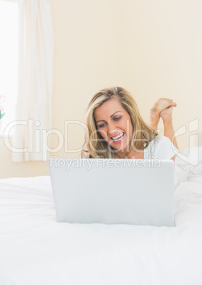 Amused woman using a laptop lying on her bed
