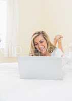 Amused woman using a laptop lying on her bed