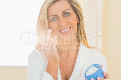 Pleased woman holding a jar of face cream in a hand and applying