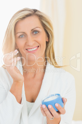 Joyful woman holding a jar of face cream in a hand and applying