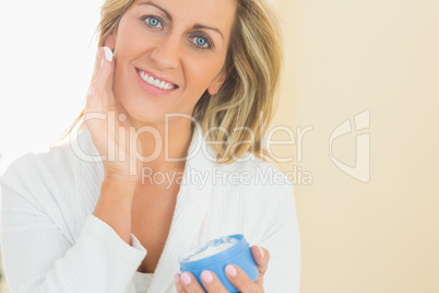 Pleased woman holding a jar of face cream in a hand and applying