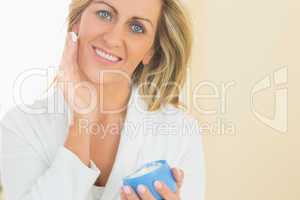 Pleased woman holding a jar of face cream in a hand and applying