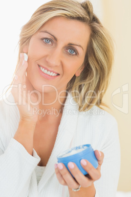 Happy woman holding a jar of face cream in a hand and applying c