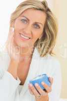 Happy woman holding a jar of face cream in a hand and applying c