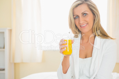 Cheerful woman looking at camera enjoying a glass of orange juic