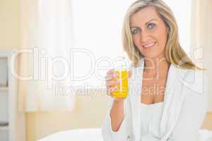 Cheerful woman looking at camera enjoying a glass of orange juic