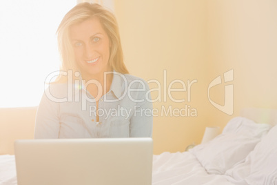 Happy woman sitting on a bed using her laptop