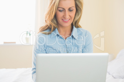 Thoughtful woman sitting on a bed using her laptop