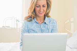 Thoughtful woman sitting on a bed using her laptop