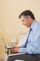 Concentrated man using a laptop sitting on a bed