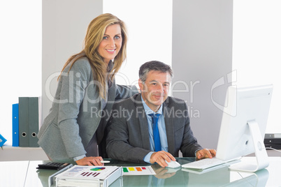 Two satisfied businesspeople looking at camera using a computer
