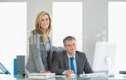 Two joyful businesspeople looking at camera using a computer