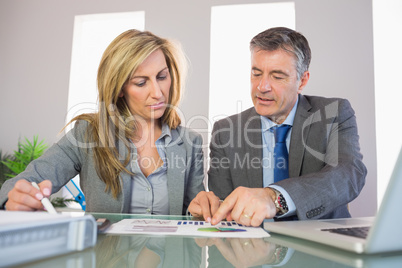 Two unsmiling business people pointing at a graphic