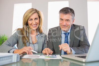 Two pleased business people smiling at camera analysing a graphi