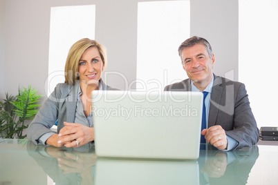 Two smiling business people looking at camera behind a laptop