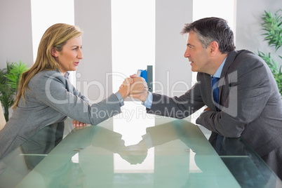 Two irritated businesspeople having an arm wrestling sitting aro