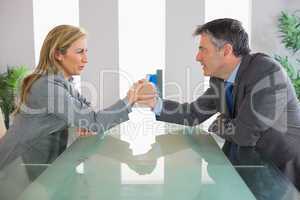 Two irritated businesspeople having an arm wrestling sitting aro