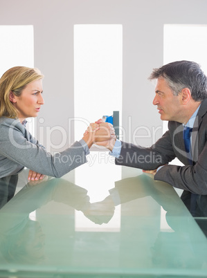 Two annoyed businesspeople having an arm wrestling sitting aroun
