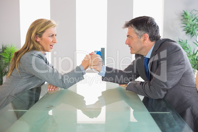 Two upset businesspeople having an arm wrestling sitting around