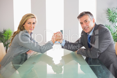 Two serious businesspeople having an arm wrestling sitting aroun