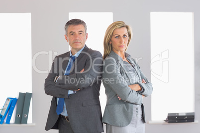 Two unsmiling businesspeople looking at camera standing back to