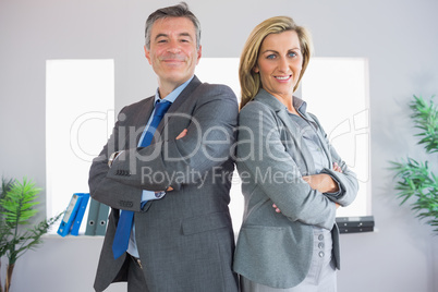Two happy businesspeople looking at camera standing back to back