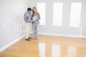 Serious blonde realtor showing a room and some documents to a po