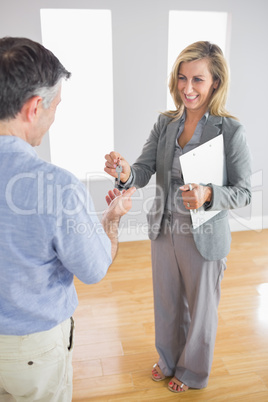 Laughing realtor holding a briefcase and giving a key to a buyer
