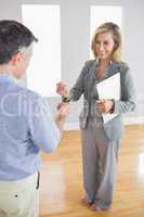 Laughing realtor holding a briefcase and giving a key to a buyer