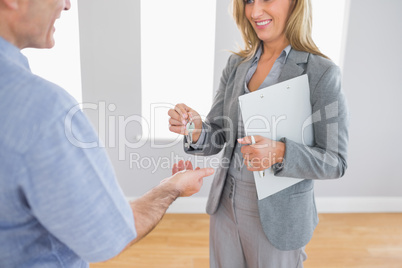Close up of a smiling realtor delivering a key to a laughing buy