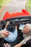 Mature couple in red convertible looking at camera