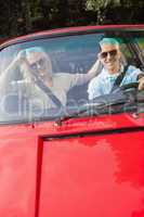 Mature couple in red cabriolet smiling at camera