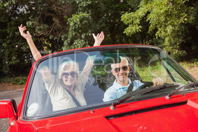 Mature couple in red cabriolet cheering at camera