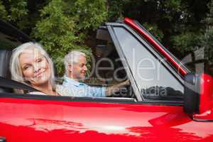 Side view of mature couple driving red convertible
