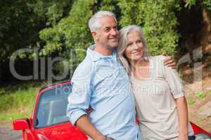 Happy mature couple posing by their red convertible