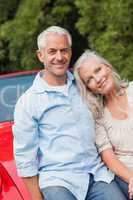 Cheerful mature couple sitting on their red convertible