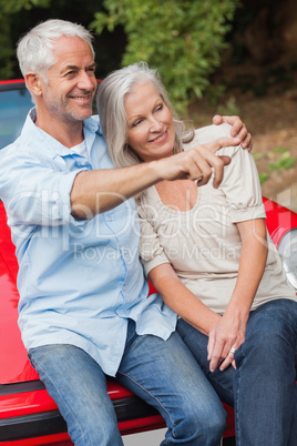 Smiling mature couple sitting on their red convertible