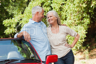 Smiling mature couple hugging by their red cabriolet
