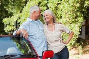 Smiling mature couple hugging by their red cabriolet