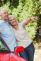 Mature couple leaning against their red cabriolet