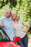 Smiling mature couple leaning against their red cabriolet