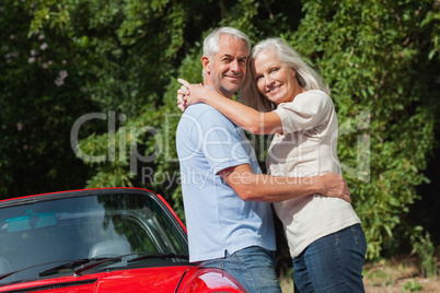 Smiling mature couple hugging against their red cabriolet