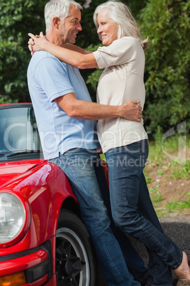 Happy mature couple hugging against their red cabriolet