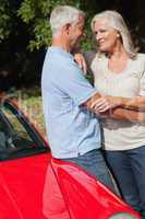 Cheerful mature couple hugging against their red cabriolet