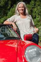 Smiling mature woman leaning against her red cabriolet